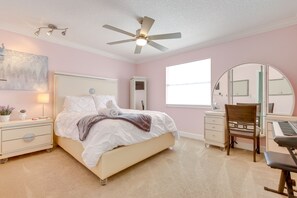 Ein Schlafzimmer mit einem Bett, einem Schreibtisch mit Tastatur, einem Stuhl, einem Deckenventilator und einem großen Fenster.