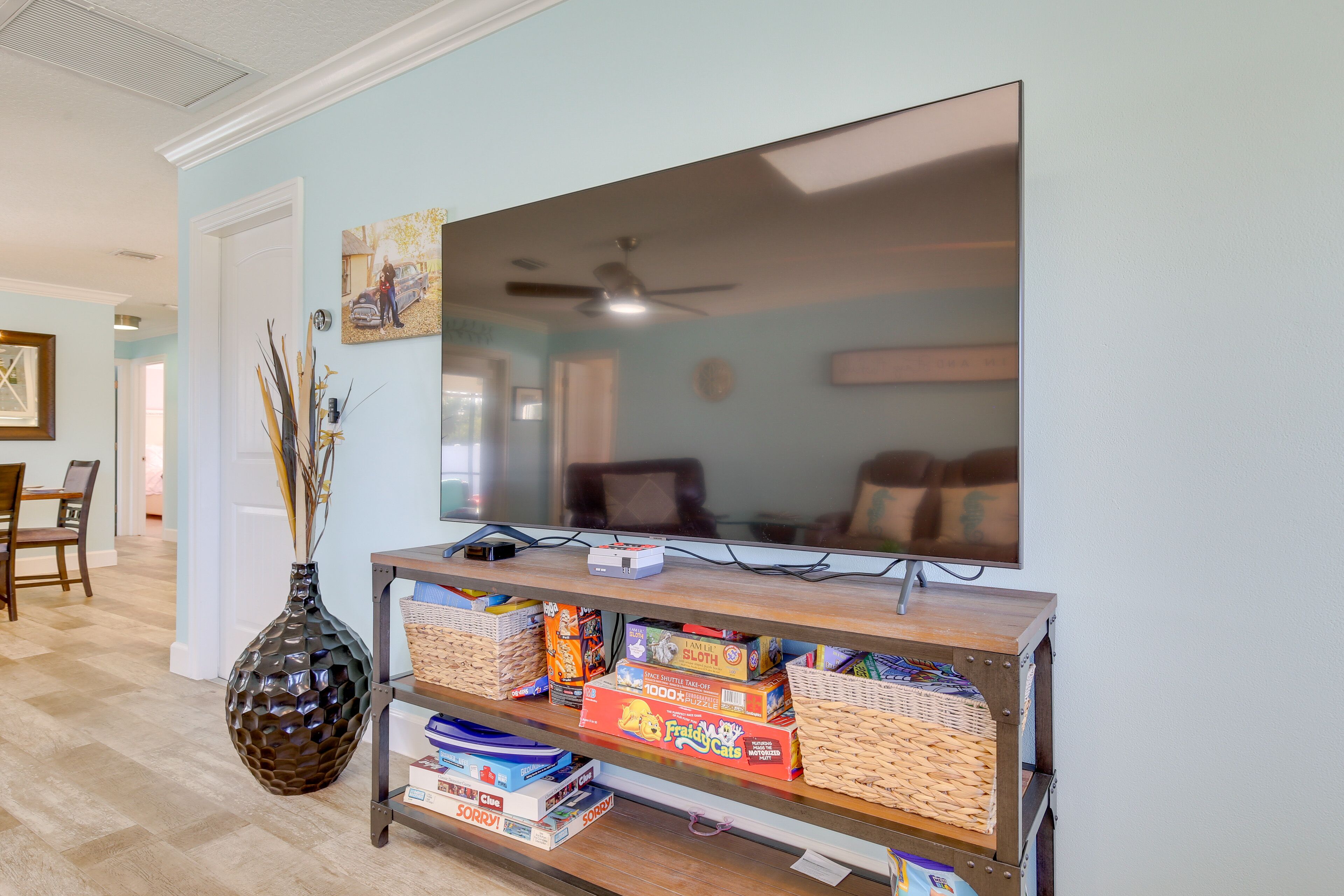 Een woonkamer met een grote flatscreen televisie op een houten standaard, een decoratieve vaas, en planken met gezelschapsspellen.