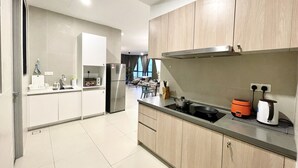 A modern kitchen with a built-in oven, a refrigerator, and a sink. There is a dining area with a table and chairs visible in the background. - KL Gateway Premium Residences by MOKA (Kuala Lumpur)