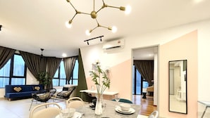 A modern dining area with a marble table set for four, a vase with a plant, and a city view through large windows. - KL Gateway Premium Residences by MOKA (Kuala Lumpur)