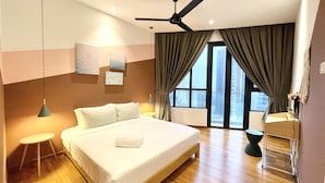 A modern hotel room with a large bed, a ceiling fan, a small bedside table, a nightstand, and a view of the city through large windows. - KL Gateway Premium Residences by MOKA (Kuala Lumpur)