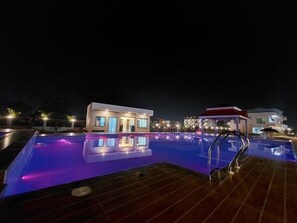 A nighttime view of a swimming pool area with a modern building in the background. - Llyods Beach Resort (Kanthi)