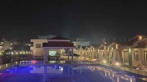 Een nachtzicht van een hotel met een zwembad, een kiosk en verlichte gebouwen.