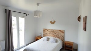 A bedroom with a bed, a bedside table, a hanging light fixture, and a view through a window with curtains. - New individual villa in Southern Corsica. (Sartène)