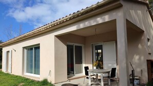 A single-story house with a covered patio, large sliding glass doors, and a small garden area. - New individual villa in Southern Corsica. (Sartène)
