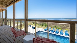 Un pontile in legno con piscina, sedie rosse e vista sulla spiaggia e sull'oceano.