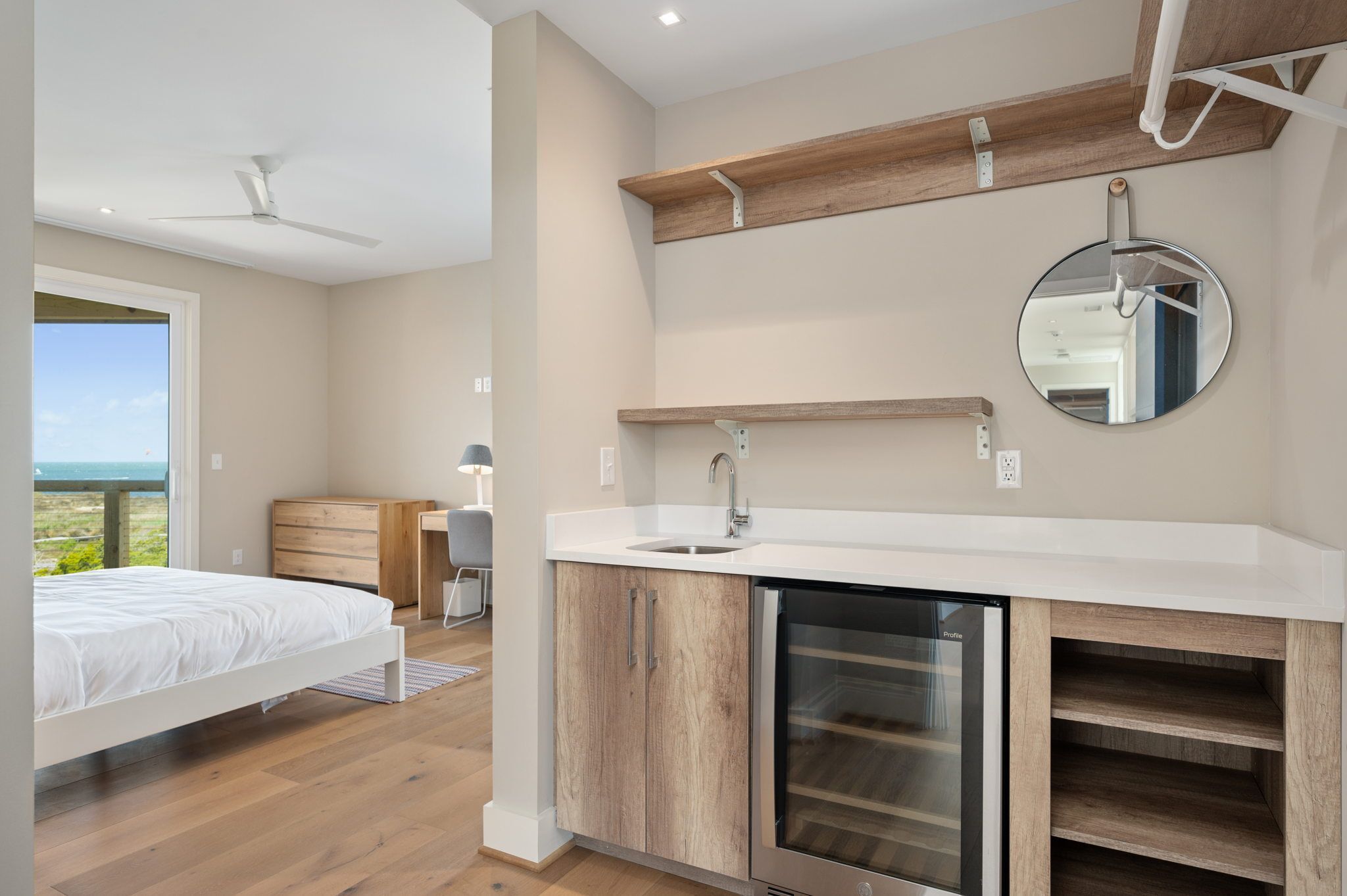 A modern bedroom with a bed, a wooden dresser, a built-in sink, and a compact refrigerator.