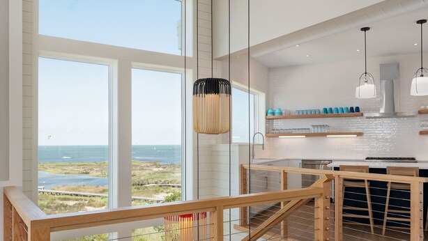 Una cucina moderna con ampie finestre, una scala in legno e vista sulla spiaggia.