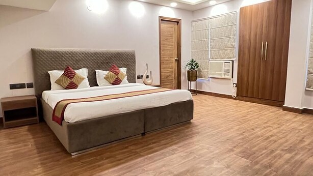 A modern hotel room with a large bed, wooden flooring, a wardrobe, and a window with blinds. - The Dream House (New Delhi)