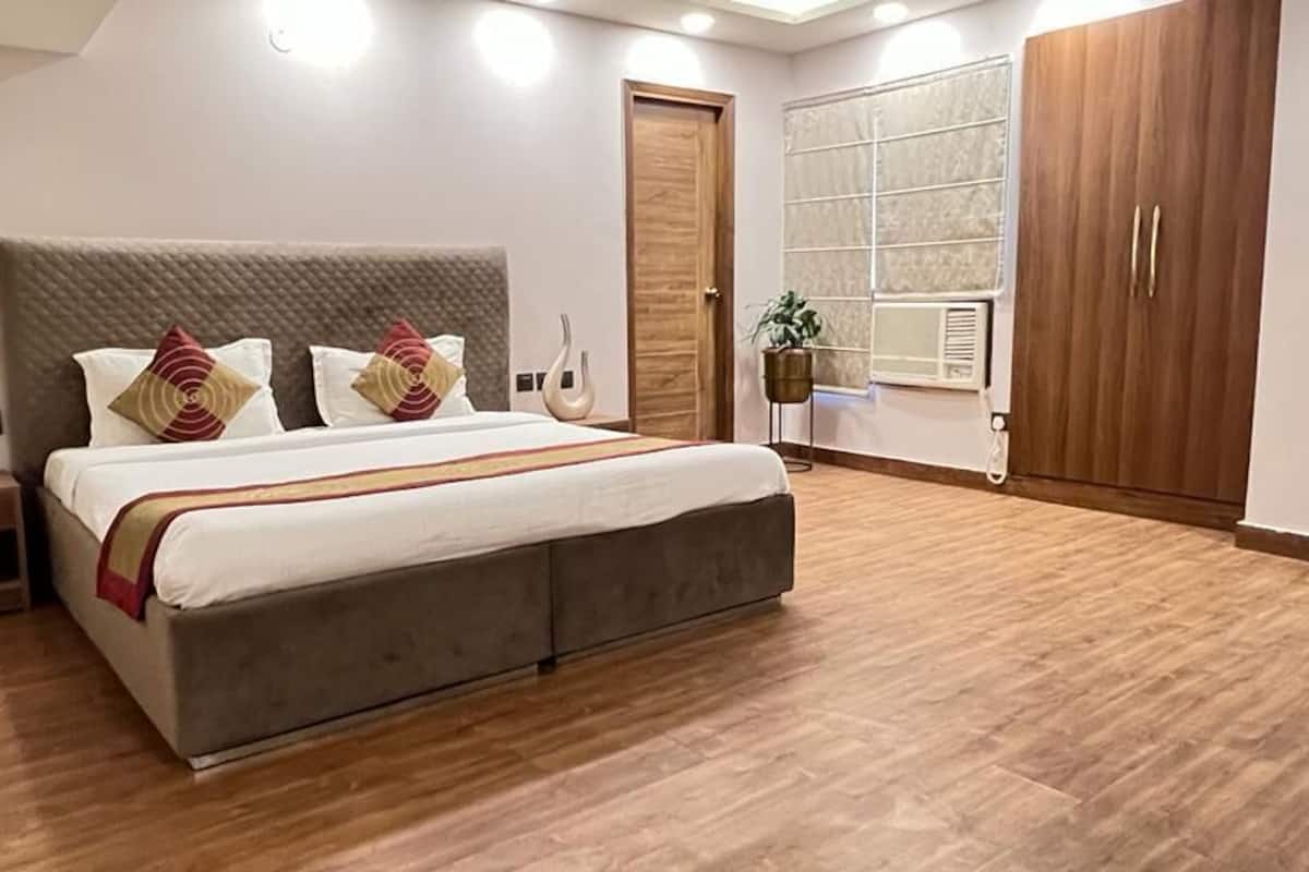 Una habitación de hotel moderna con una cama grande, suelo de madera, un armario y una ventana con persianas.