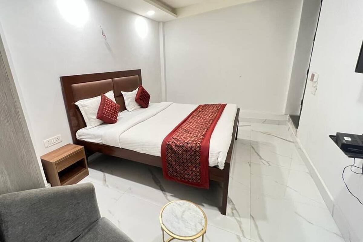 Una habitación de hotel moderna con una cama grande, una mesita de noche, una pequeña mesa redonda y un sillón gris.