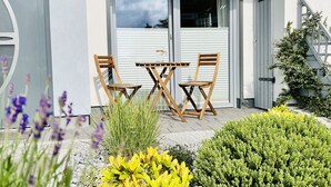 A modern house with a garage door marked '17A', a patio with a table and chairs, and a well-maintained garden with various plants.