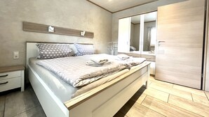 A modern bedroom with a large bed, a wardrobe, and a mirror.