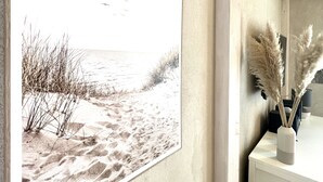 A framed beach scene with birds, pampas grass, and a vase on a white table.