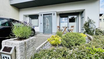 Un bâtiment moderne avec une porte grise, une petite table avec deux chaises et une voiture garée à proximité.