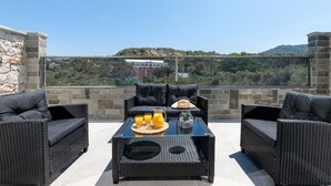 Uma área de pátio com móveis de vime, uma mesa de vidro e vista para uma encosta.
