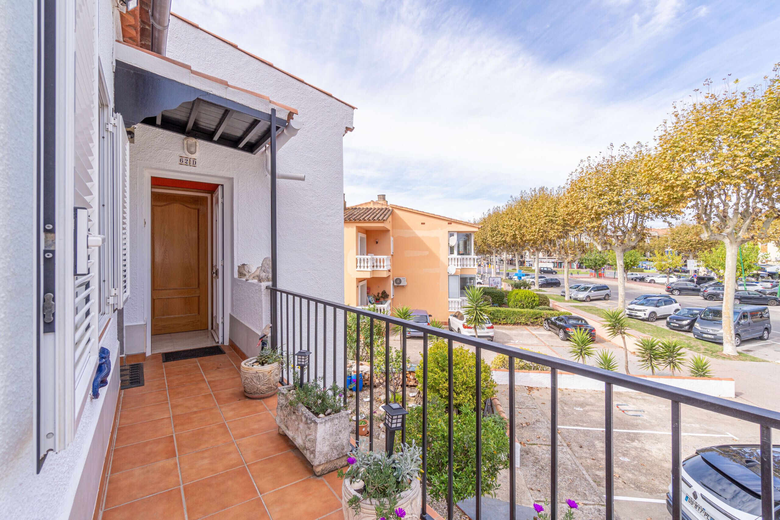Un balcon doté d’un sol carrelé, de plantes en pot et offrant une vue sur un parking et des immeubles.