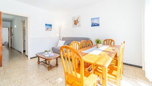 A dining area with a wooden table and chairs, a grey sofa, and a small side table with a lamp.