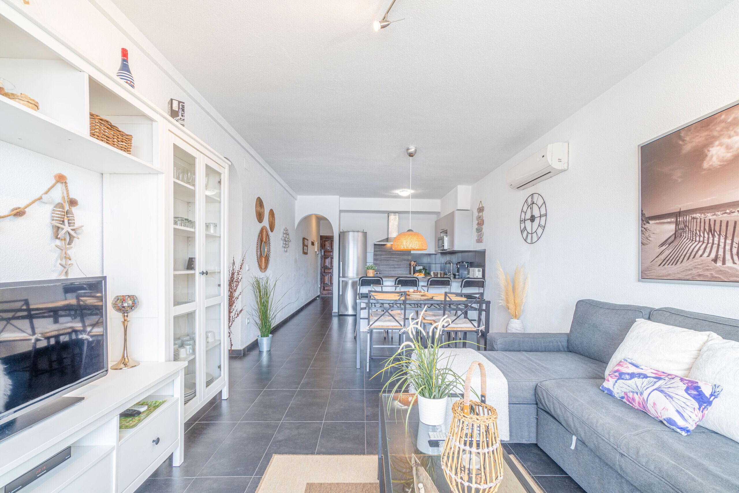Un salon moderne avec un canapé gris, un téléviseur à écran plat et un coin repas comprenant une table et des chaises.
