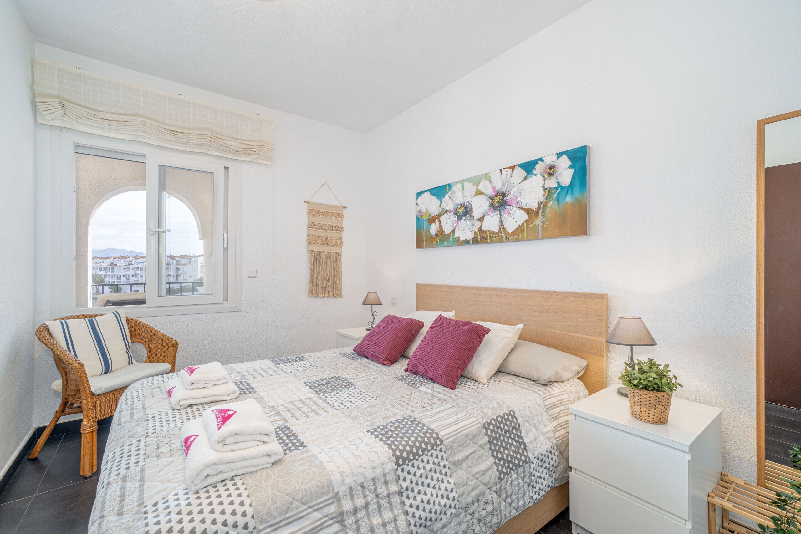 A bedroom with a bed, a chair, a nightstand, a lamp, a painting, and a window with a view.