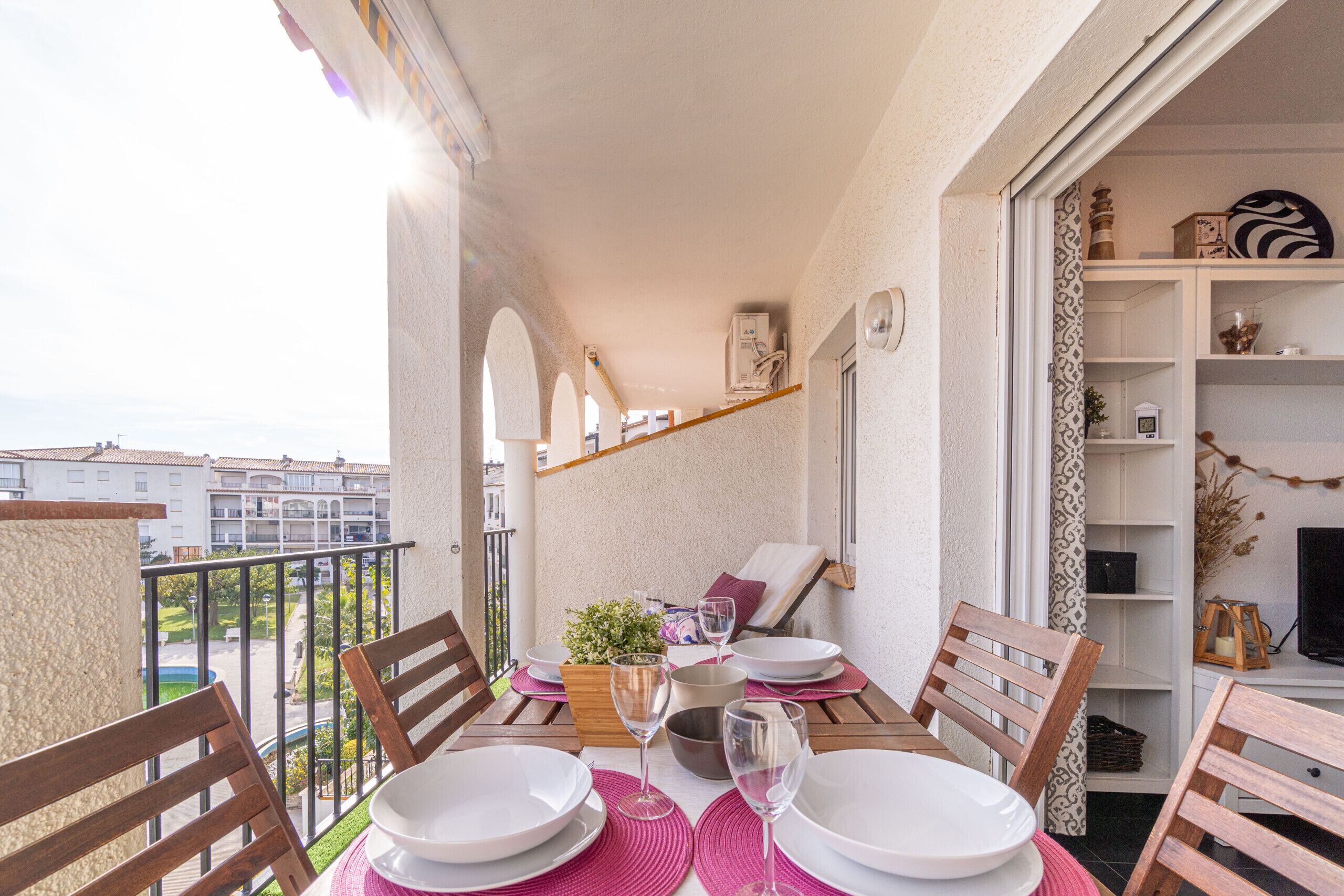 A balcony with a dining table set for two, a potted plant, and a view of the surrounding buildings.