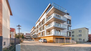 Un immeuble résidentiel à plusieurs étages, doté de balcons, situé le long d’une rue pavée, avec une voiture garée.