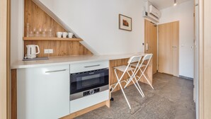 Une cuisine moderne équipée d’un four Bosch, d’une bouilloire et d’une machine à café sur le plan de travail. On y trouve également deux chaises blanches et une étagère en bois avec des verres.
