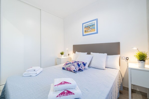 A neatly made bed with a floral pillow, white towels, and a framed picture on the wall.