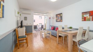 A modern living room with a sofa, dining table, chairs, and a coffee table. There is a TV on a stand, a plant, and artwork on the walls.