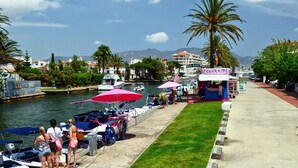 A marina with boats docked, a food kiosk, and a palm tree.