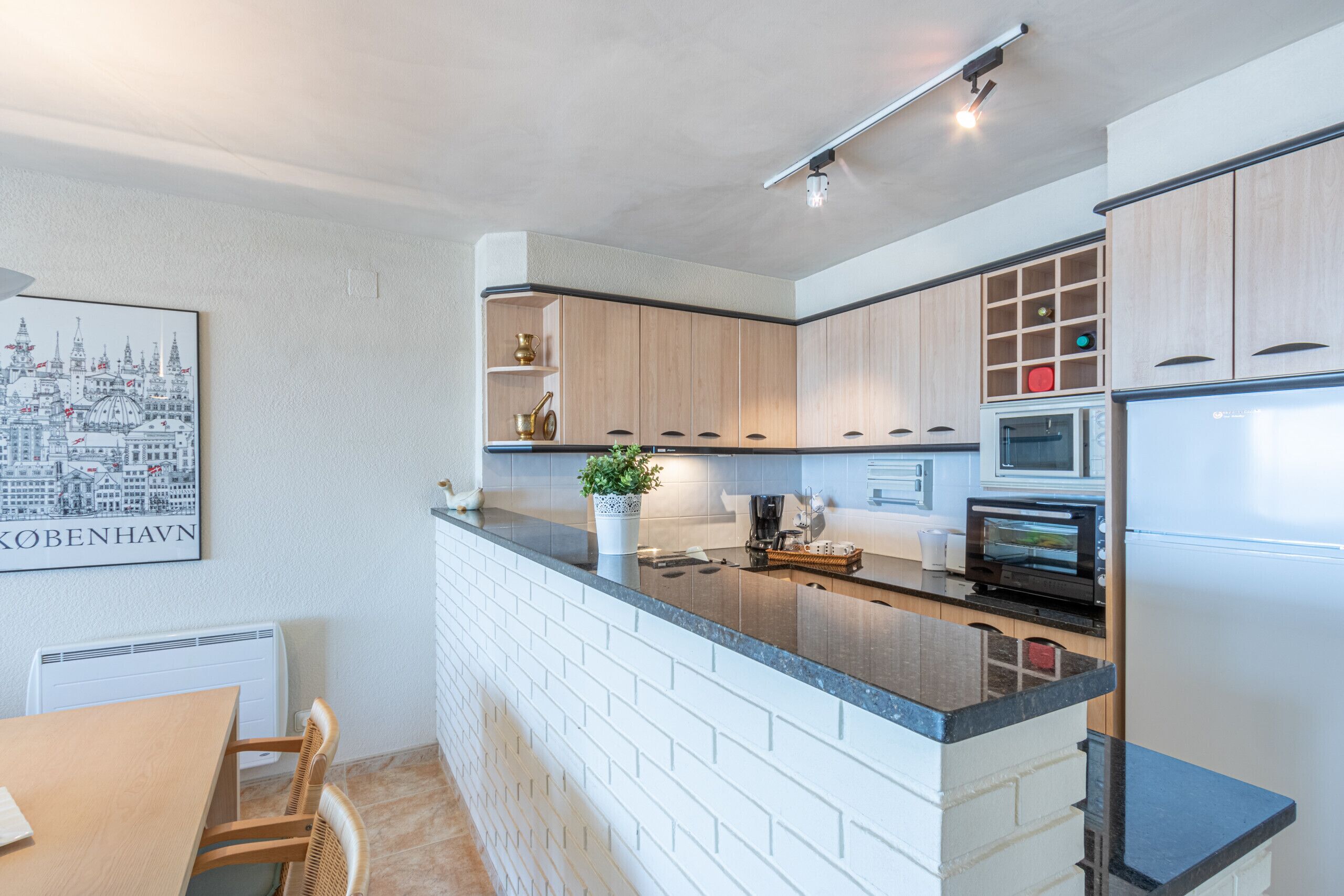 Une cuisine moderne avec un îlot central en briques, des armoires en bois et une œuvre d’art représentant un paysage urbain accrochée au mur.