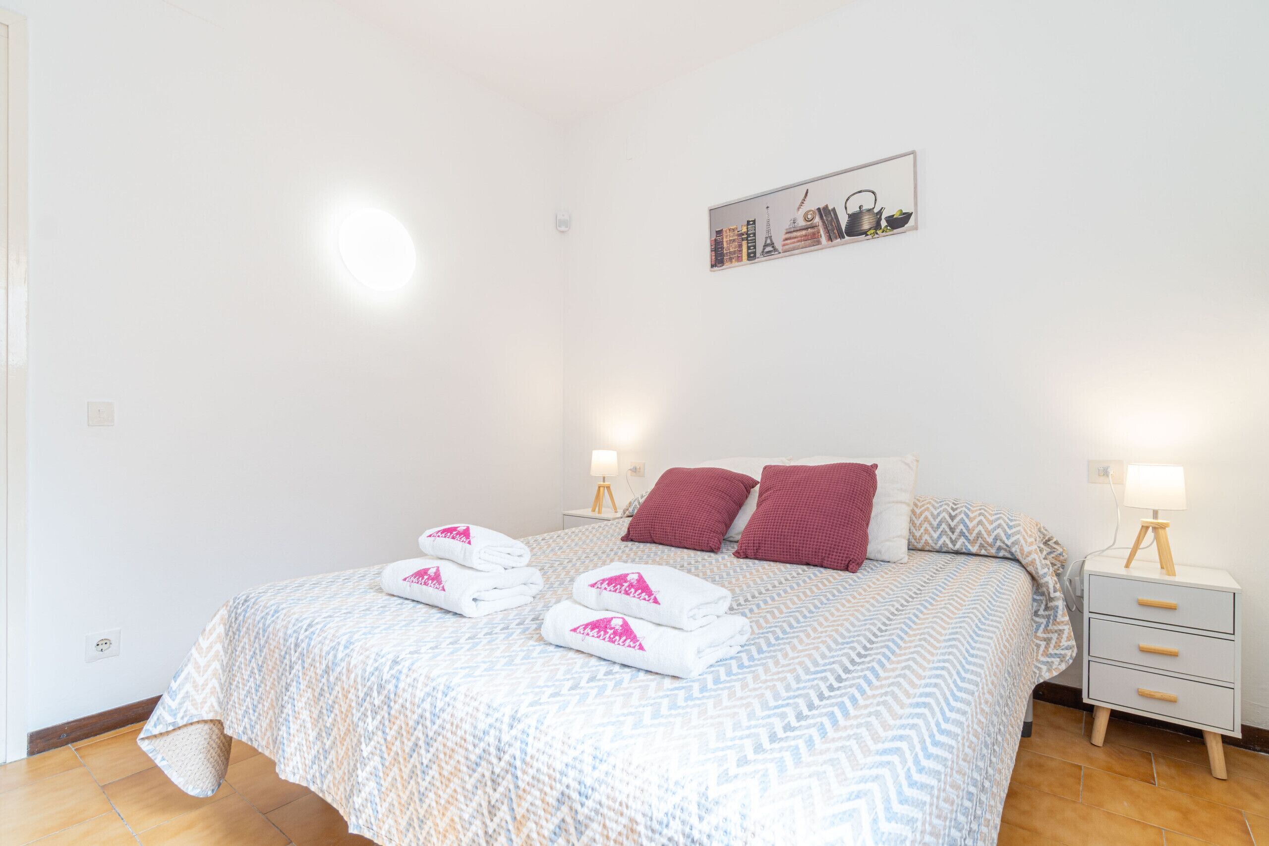 A neatly made bed with a patterned bedspread, two pillows, and a bedside table with a lamp.