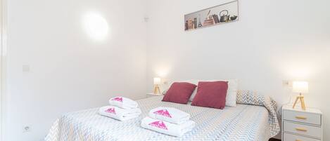 A neatly made bed with a patterned bedspread, two pillows, and a bedside table with a lamp.