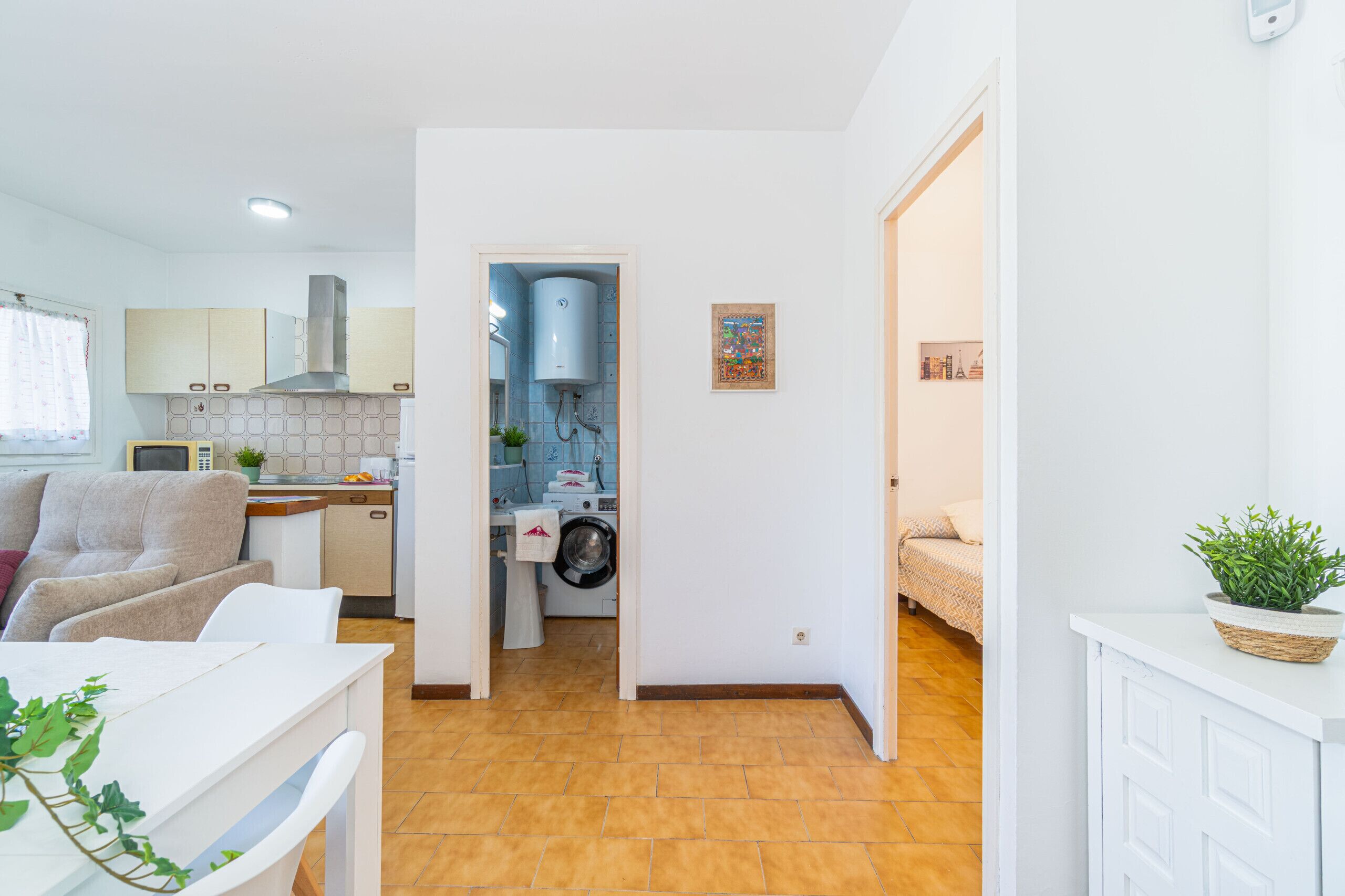 Une cuisine moderne équipée d’un lave-linge intégré, un coin repas avec une table blanche et une chambre avec un lit.