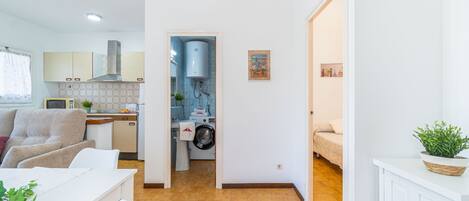 Une cuisine moderne équipée d’un lave-linge intégré, un coin repas avec une table blanche et une chambre avec un lit.