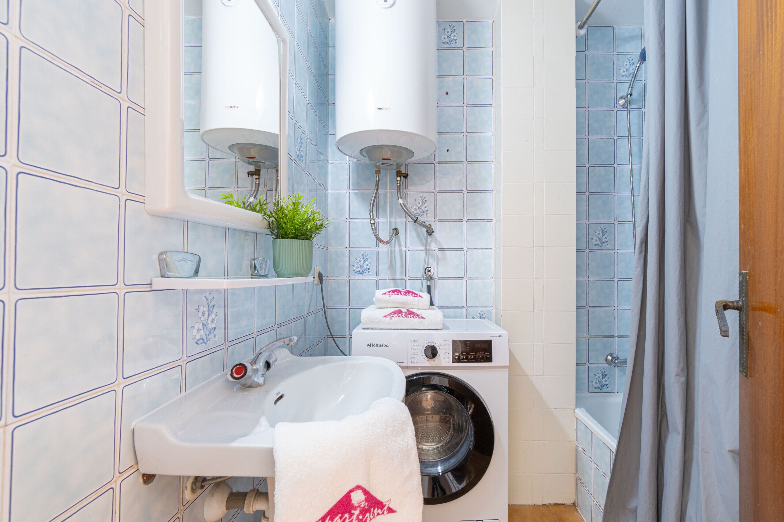 A bathroom with a sink, a washing machine, and a shower.