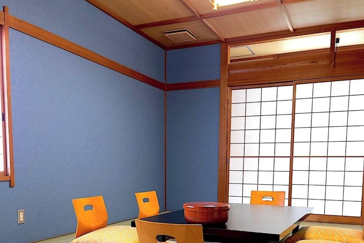 Ein Raum mit Tatami-Matten, einem niedrigen Tisch, zwei Stühlen und einem Shoji-Bildschirm.