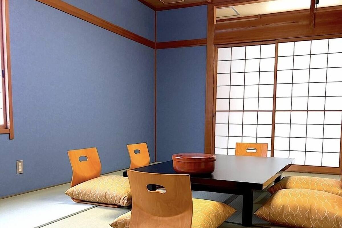 Ein Raum mit Tatami-Matten, einem niedrigen Tisch, Stühlen, einem Shoji-Bildschirm und traditioneller japanischer Einrichtung.