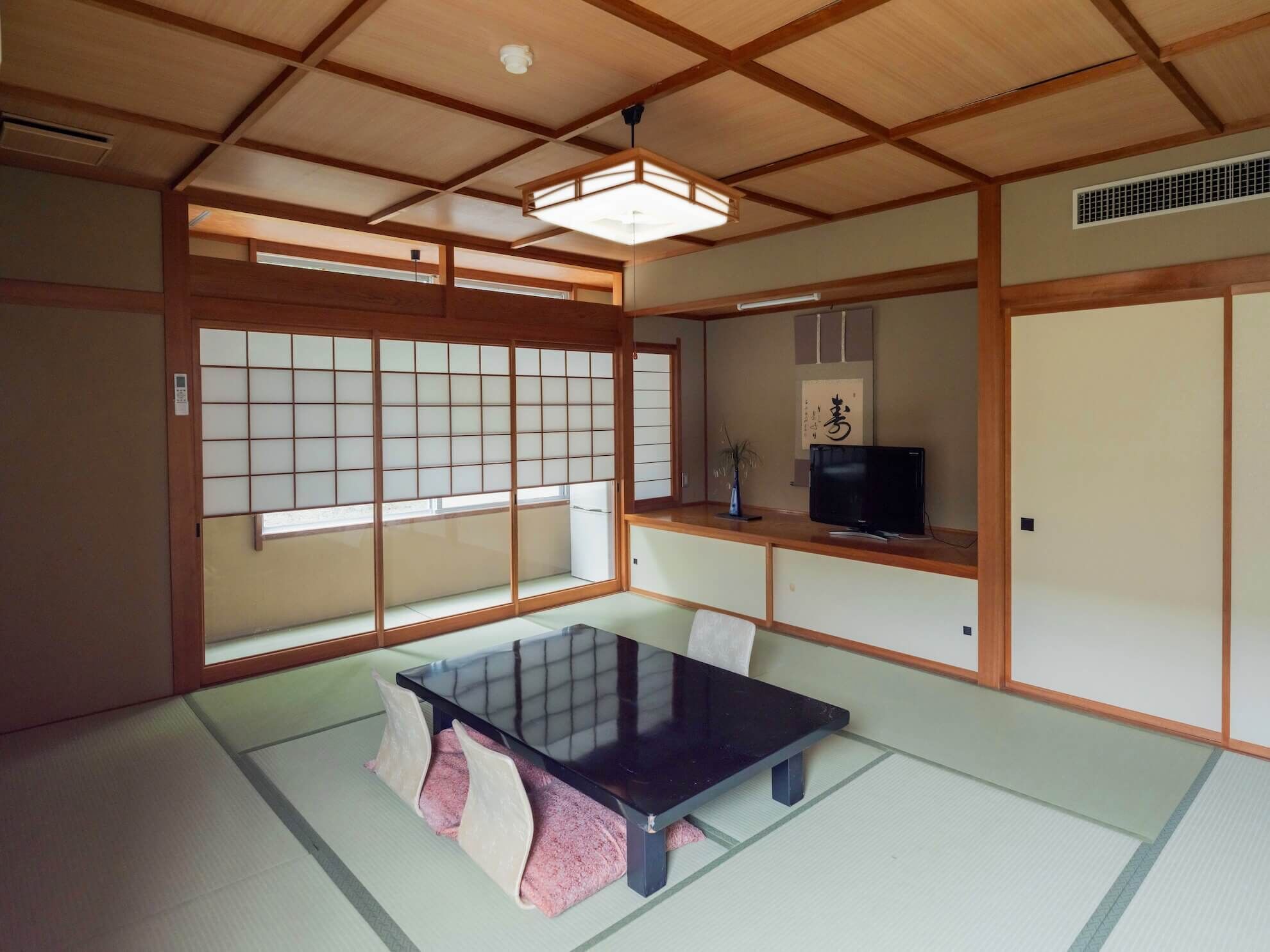 Een traditionele Japanse kamer met tatami vloerbedekking, een lage tafel, schuifdeuren en een televisie.