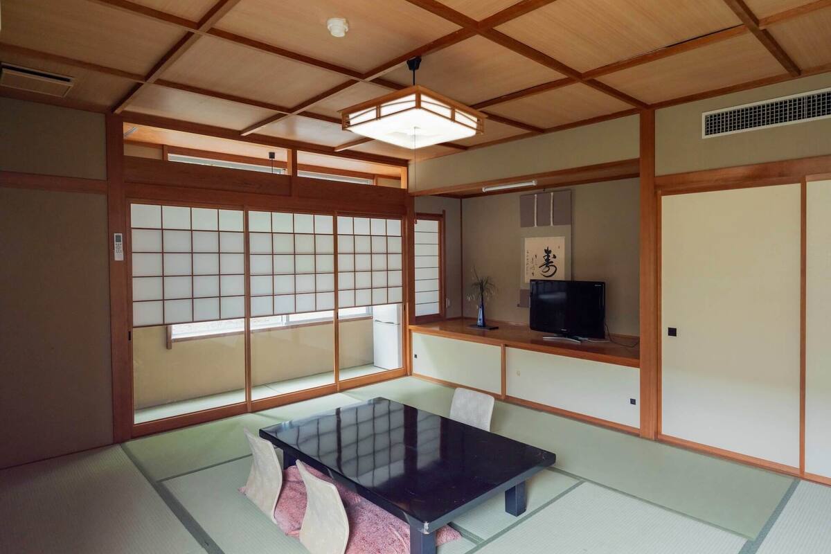 Ein traditioneller japanischer Raum mit Tatami-Böden, einem niedrigen Tisch, Schiebetüren und einem Fernseher.