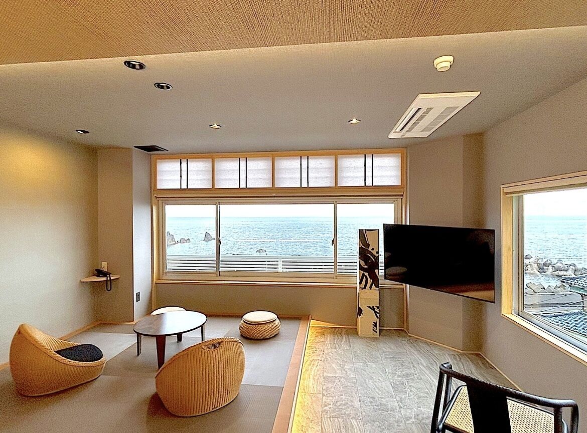 Een moderne woonkamer met een groot raam, een flatscreen televisie en uitzicht op zee.