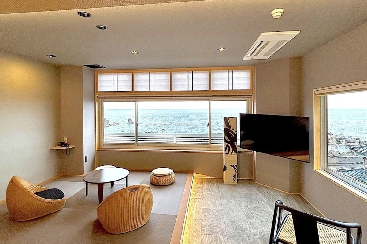 A modern living room with a large window, a flat-screen TV, and a view of the sea.