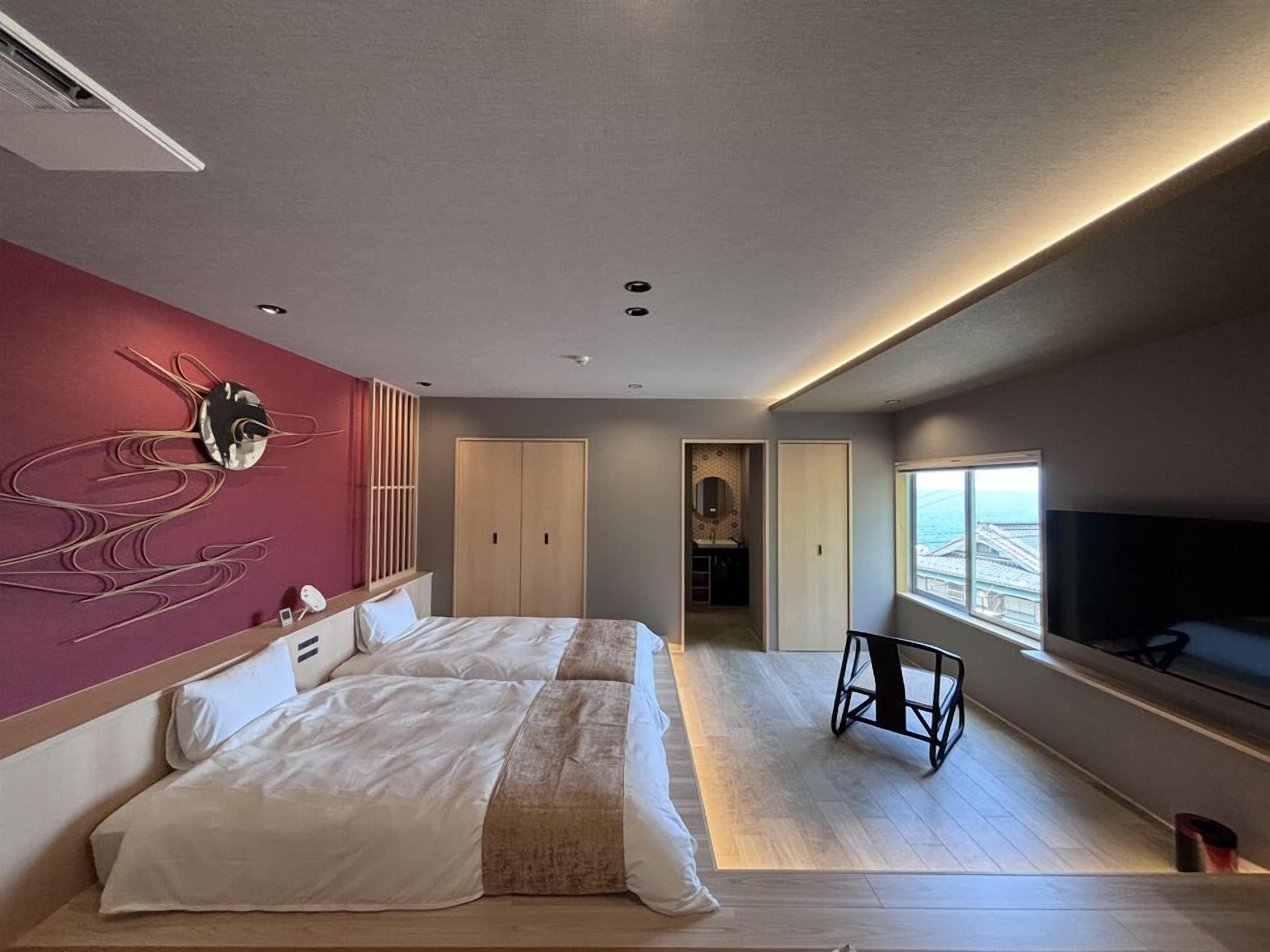 Een moderne hotelkamer met een groot bed, een televisie, uitzicht op zee en een uniek kunstwerk aan de muur.