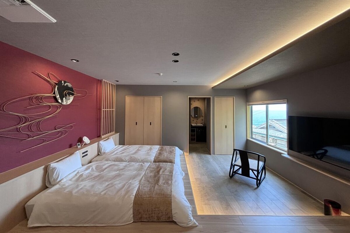 Una moderna camera d'albergo con un letto grande, una TV, vista mare e un'opera d'arte originale al muro.