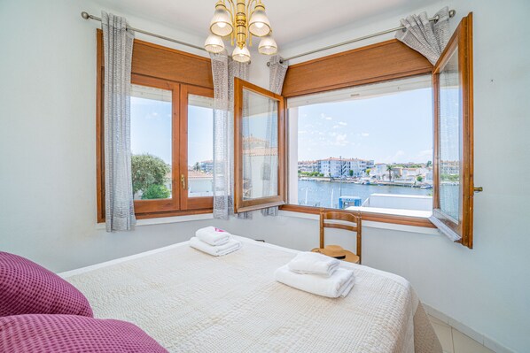 A hotel room with a bed, a chair, and a view of a cityscape and water.