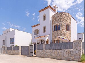 Una casa de dos pisos con fachada de piedra, un balcón y un acceso con portón.