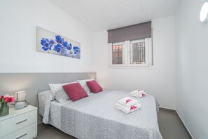 Ein Schlafzimmer mit Bett, Kissen, Nachttisch, Lampe, Fenster und einem Gemälde.