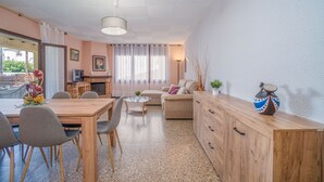 A modern living room with a wooden dining table, grey chairs, a sofa, and a wooden cabinet.