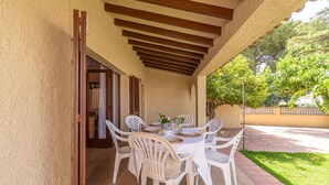 A covered patio with a table set for four, surrounded by white plastic chairs.