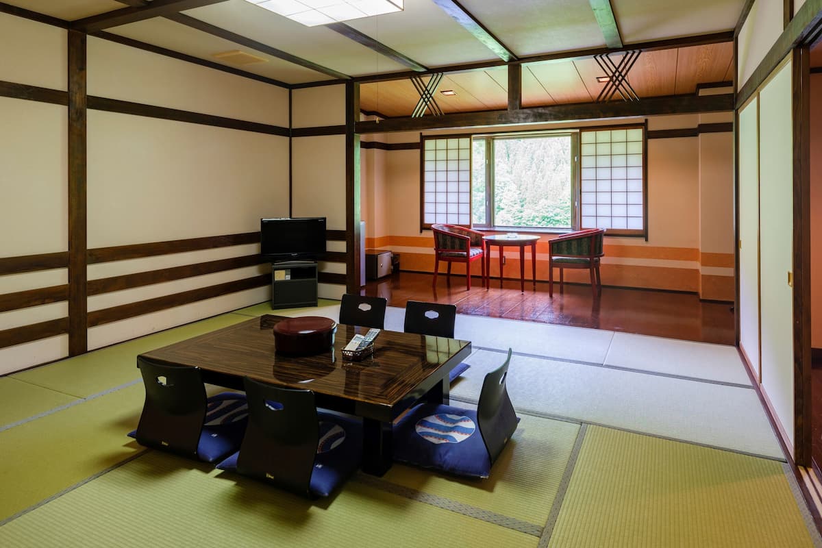 A tatami mat room with a traditional Japanese-style table and chairs, a television, and sliding doors leading to another room.